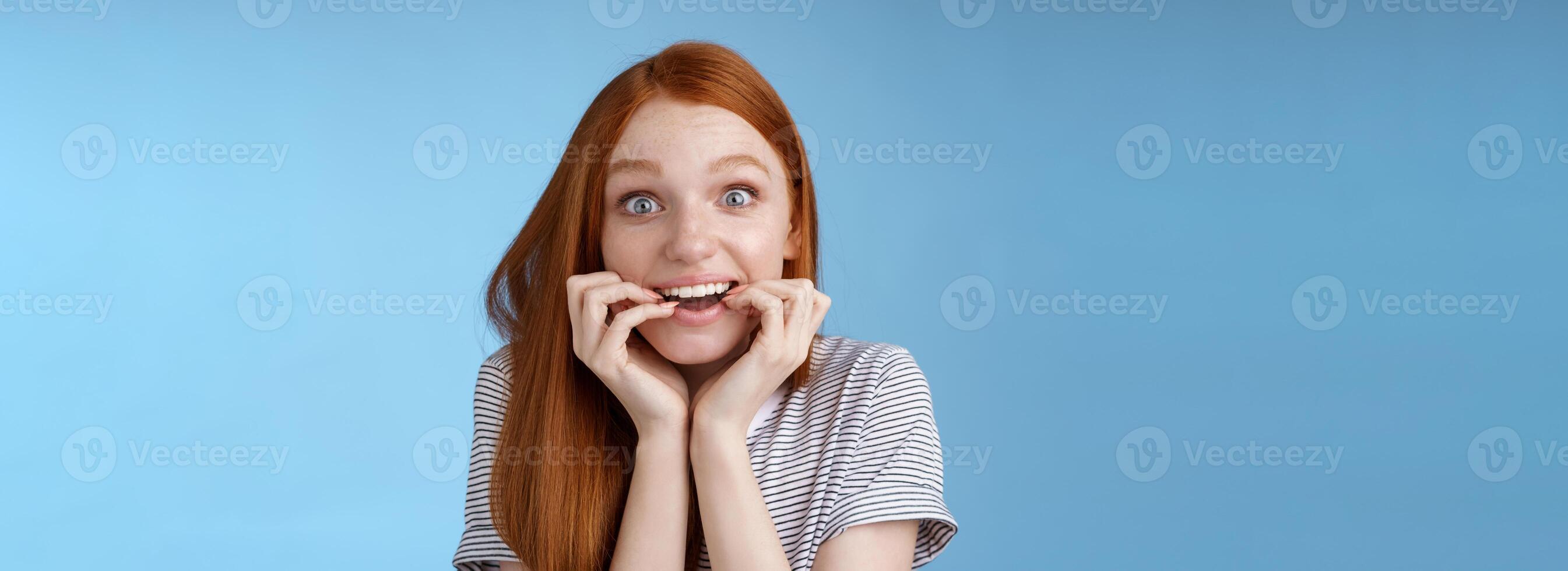 opgewonden versteld staan aantrekkelijk roodharige meisje blauw ogen kijken gefascineerd genegenheid glimlachen verlangen beet vingernagels gretig voelen verbaasd kan niet wacht beet smakelijk voedsel, staand blauw achtergrond opgewonden foto