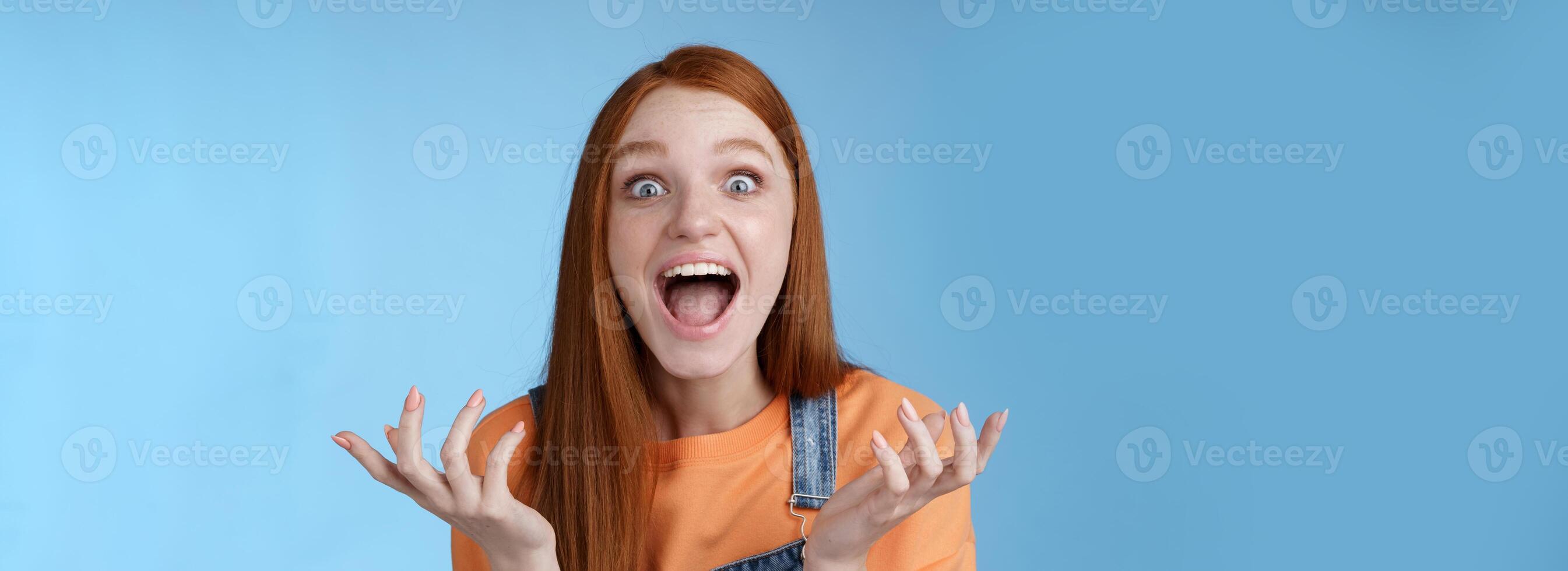 extreem gelukkig mooi Kaukasisch roodharige meisje reageren geweldig fantastisch nieuws geschreeuw opgewonden verhogen handen geamuseerd beven gelukkig schreeuwen Ja kijken verrast verbaasd, blauw achtergrond foto