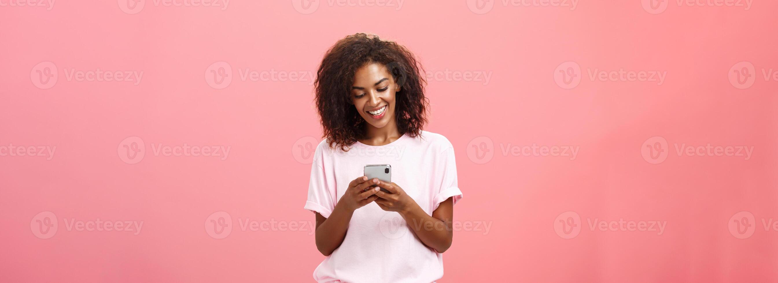 meisje schrijven tekst bericht naar vriend. portret van charmant geamuseerd en gelukkig jong met een donkere huid vrouw met gekruld haar- op zoek Bij smartphone scherm typen glimlachen genieten van koel Kenmerken van mobiele telefoon foto