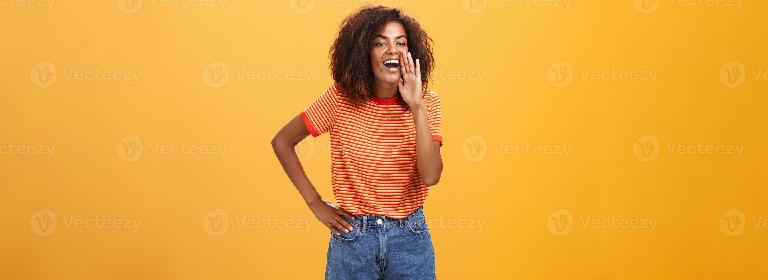 meisje roeping zus komen naar telefoon schreeuwen uit luid Holding palm in de buurt geopend mond naar worden schreeuw luider zo vriend kan horen Holding arm Aan taille staren links met zorgeloos verheugd kijken over- oranje muur foto