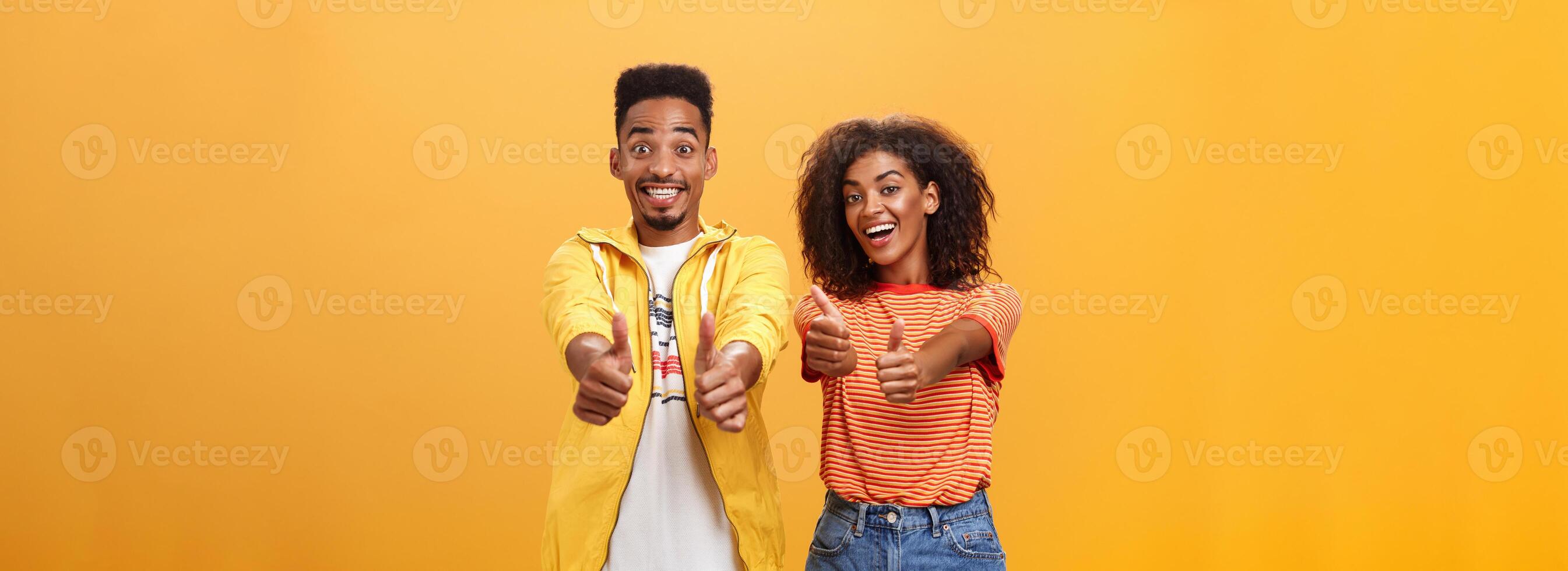 twee vrienden Leuk vinden perfect en geweldig plan. portret van blij vriendelijk ogend optimistisch Afrikaanse Amerikaans vrouw en mannetje tonen duimen omhoog in goedkeuring en overeenkomst gebaar glimlachen breed foto