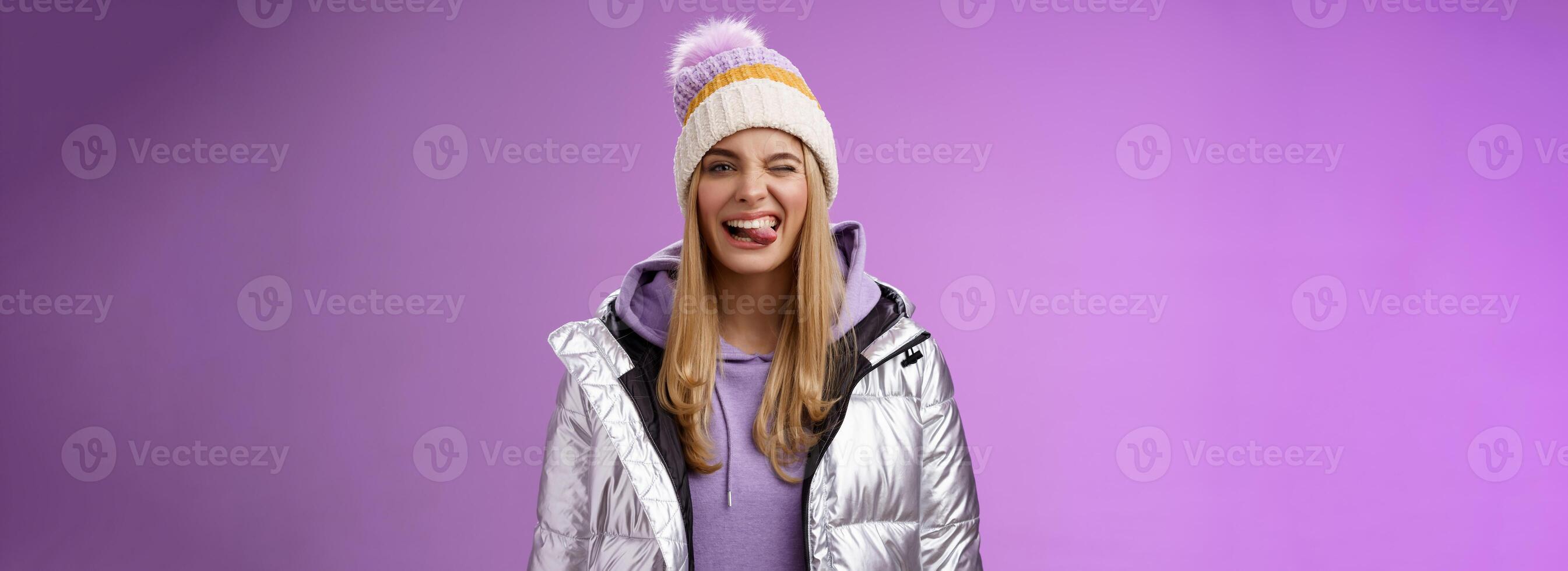 brutaal zorgeloos verheugd charmant blond meisje hebben pret voelen geamuseerd positief tonen tong glimlachen breed vervelend winter zilver glinsterende jasje elegant hoed genieten van geweldig ski vakantie foto
