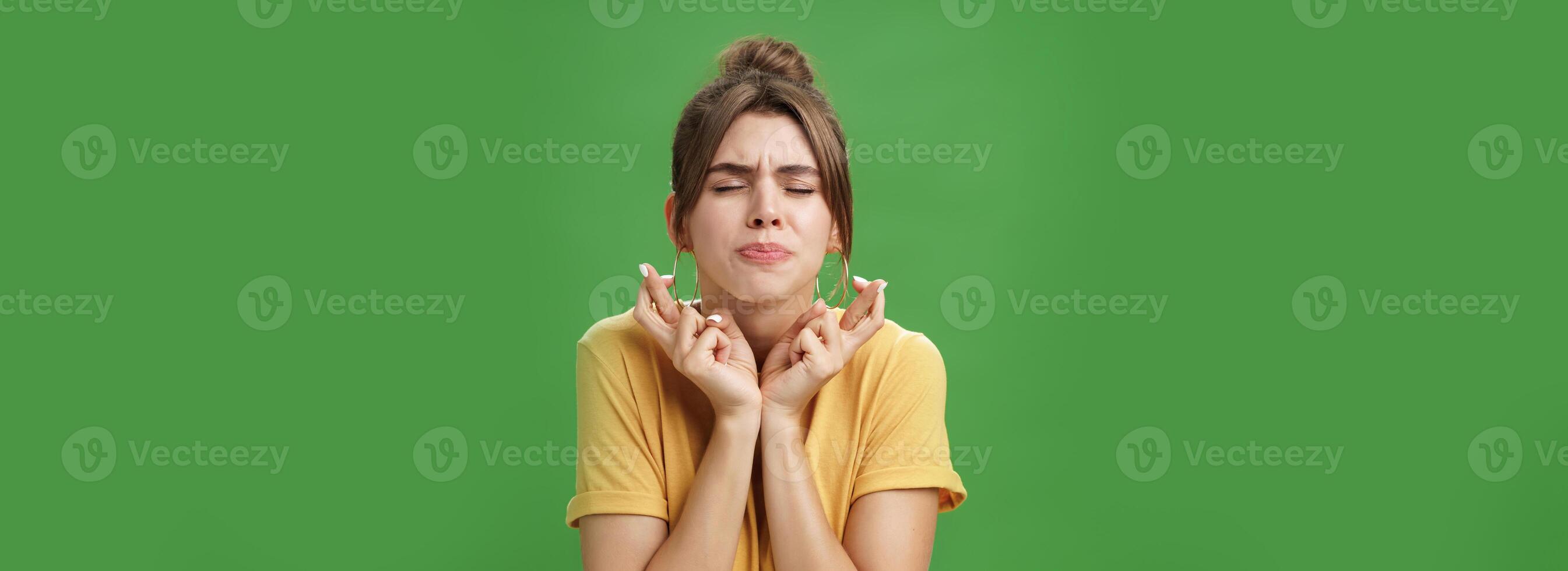 bezorgd intens, bezorgd aantrekkelijk jong Europese vrouw model- in geel t-shirt verhogen schouders kruispunt vingers voor mooi zo geluk achtervolgen lippen en sluitend ogen terwijl aan het wachten voor wonder Hopelijk foto