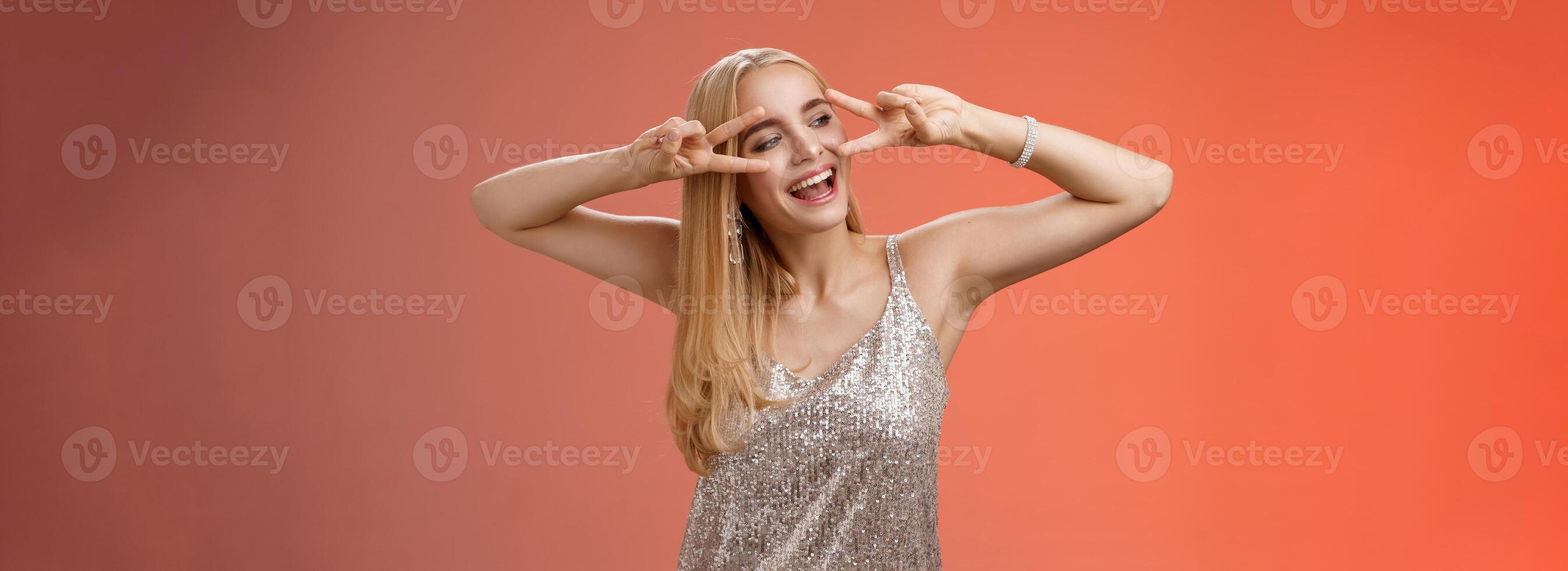 zorgeloos blij mooi fantastisch blond vrouw hebben pret vieren feesten dansen gelukkig tonen zege vrede disco tekens kijken terzijde vermaakt, genieten van geweldig muziek, rood achtergrond foto