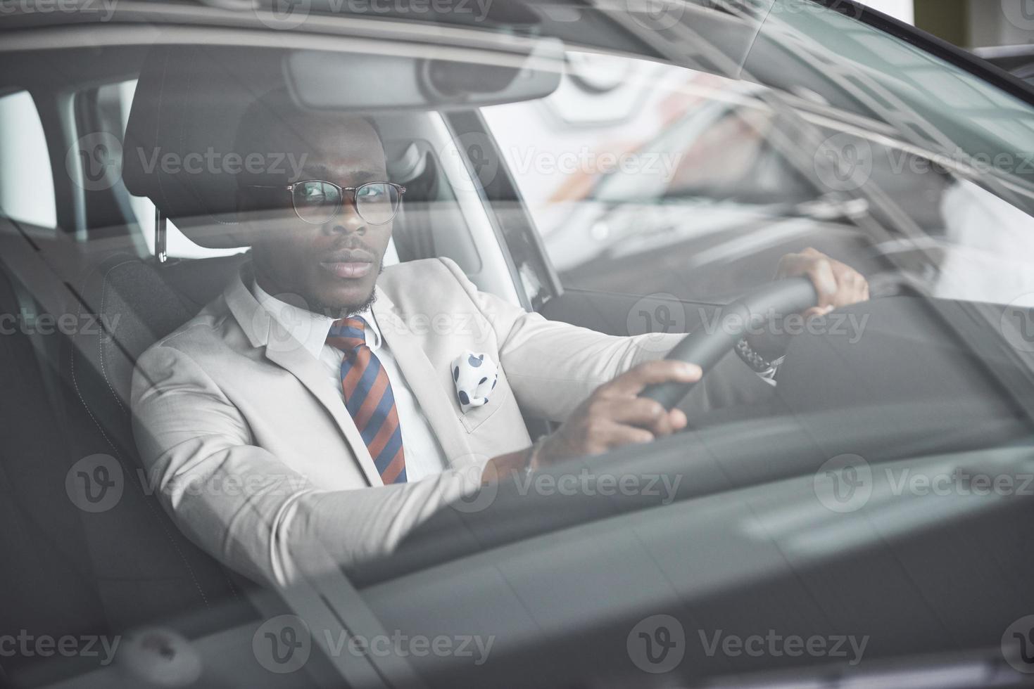 vooraanzicht van knappe Afrikaanse elegante serieuze zakenman rijdt in een auto foto