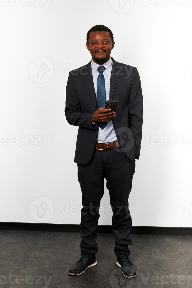glimlachen Afrikaanse Amerikaans zwart Mens in bedrijf pak met smartphone wit muur achtergrond foto