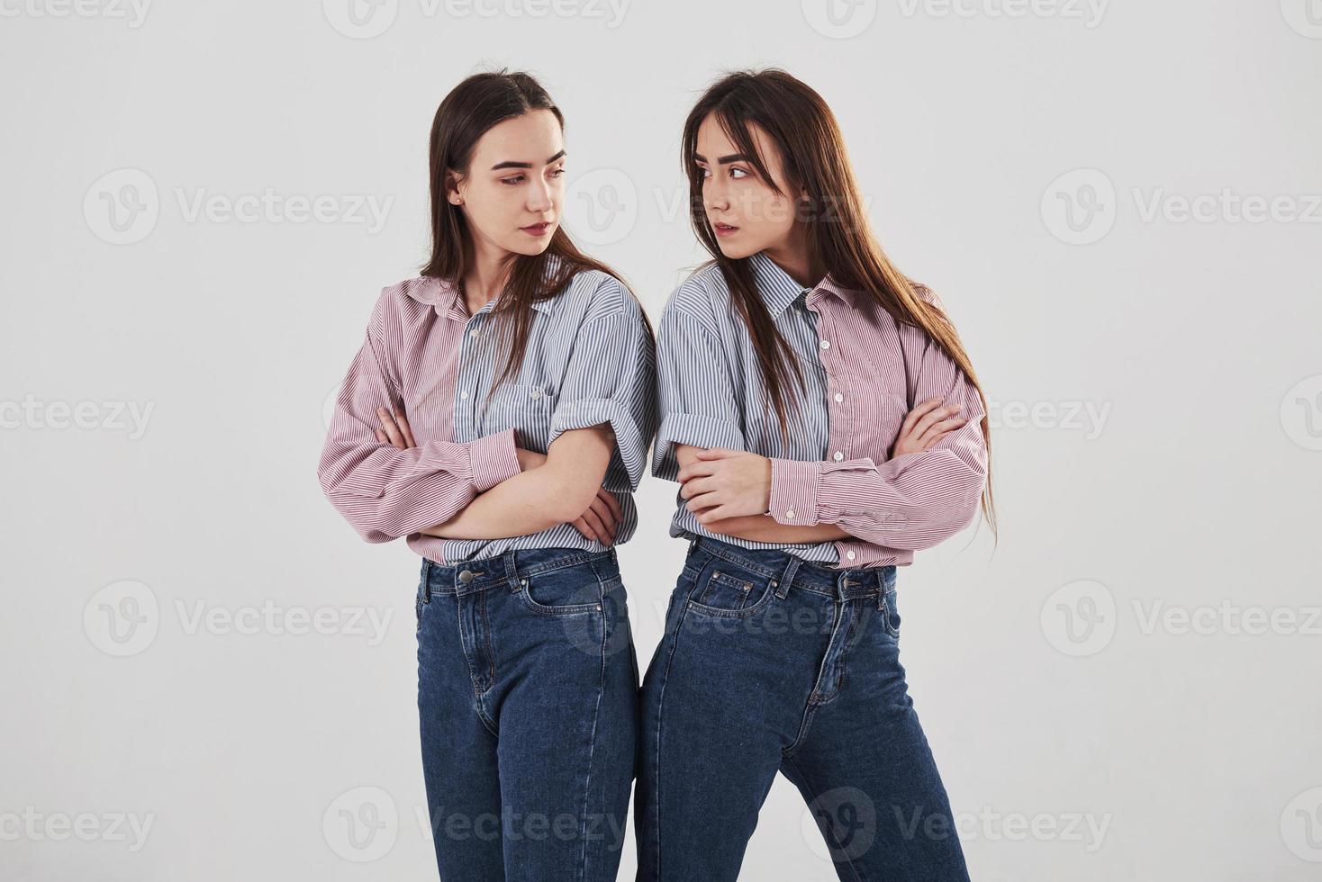 beledigd en kijk boos naar de ander. twee zussen tweeling staan en poseren in de studio met witte achtergrond foto