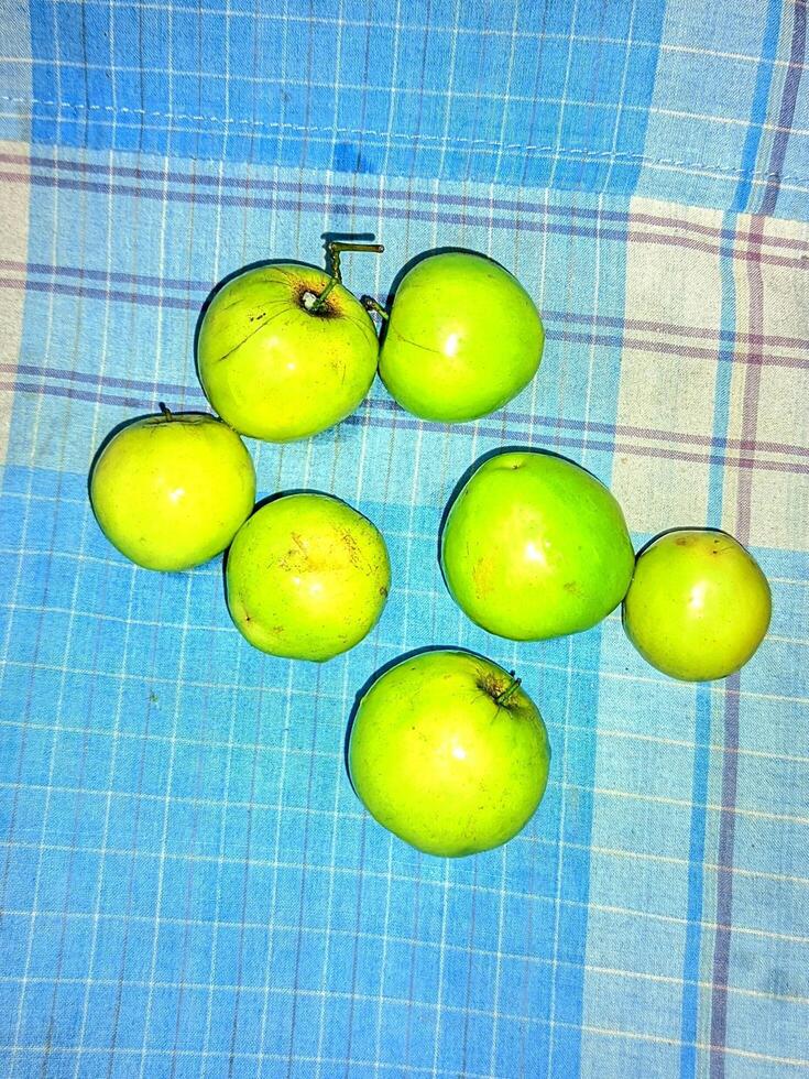 een groep van groen appels zittend Aan een blauw en wit geruit tafel kleding foto