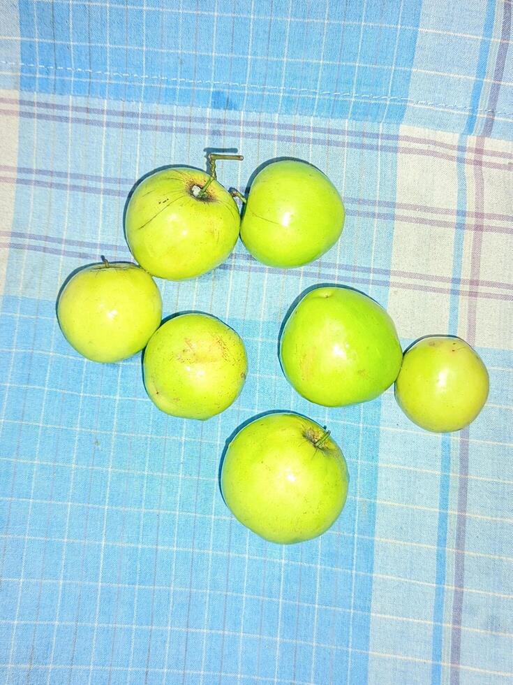 een groep van groen appels zittend Aan een blauw en wit geruit tafel kleding foto