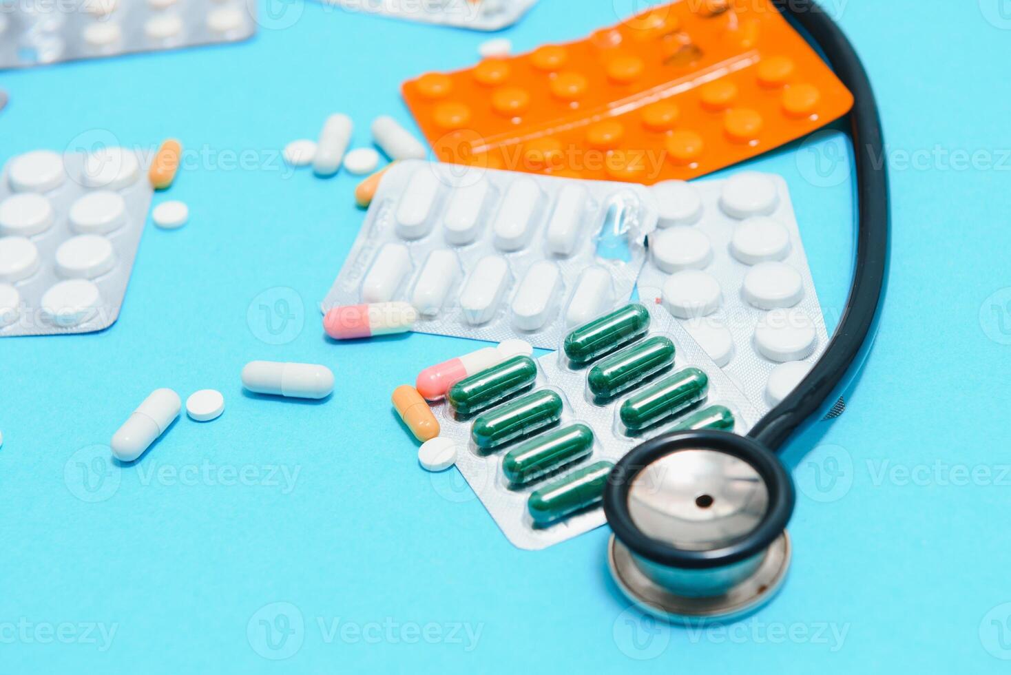 verspreide wit pillen Aan blauw tafel.medisch, apotheek en gezondheidszorg concept. blauw achtergrond wit pillen met een medisch statoscoop, top visie foto