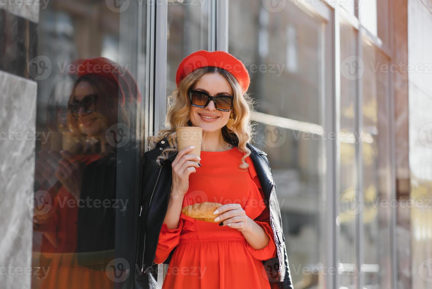 mooi gelukkig vrouw met zoet glimlach in wijnoogst zonnebril in hoed in gewoontjes rood Zwart kleren met koffie wandelingen en glimlacht buitenshuis in stad. vrolijk stedelijk mode meisje Aan wandelen in voorjaar zonnig dag. foto