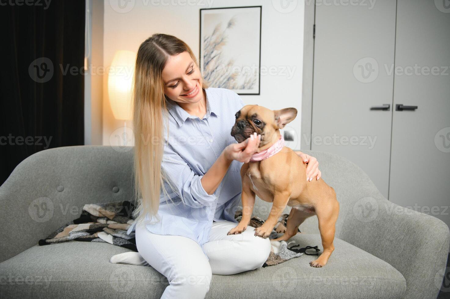 jong mooi vrouw in gewoontjes kleren knuffelen haar hond zittend Aan de sofa in de leven kamer van haar knus land huis. dier communicatie concept foto