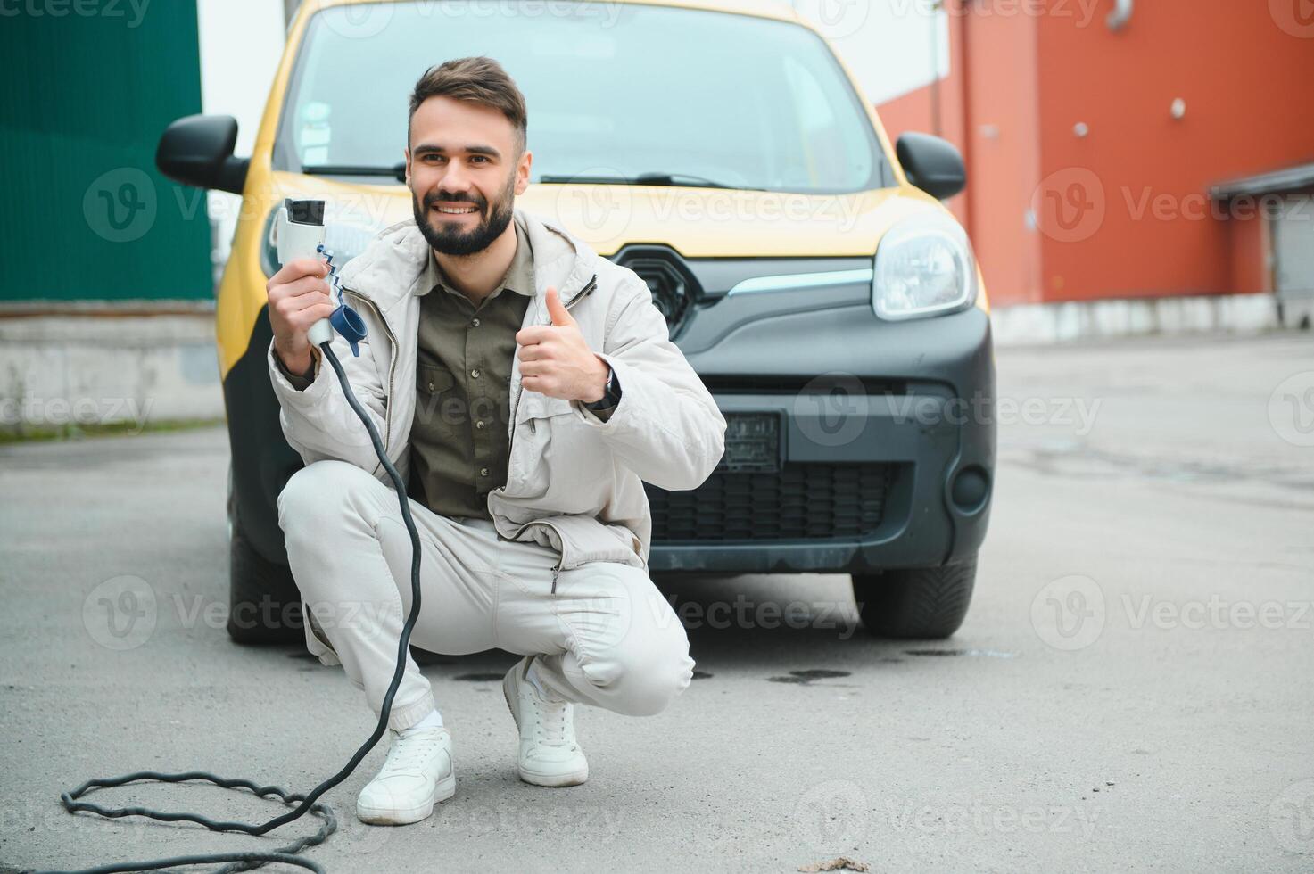 portret van een jong Mens staand met opladen kabel in de buurt de opladen station foto