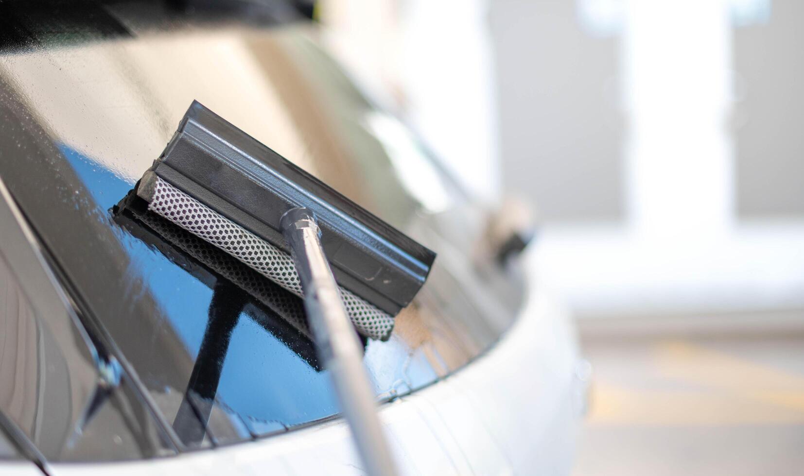 volwassen mannetje arbeider schoonmaak auto voorruit met de spons dweil. foto