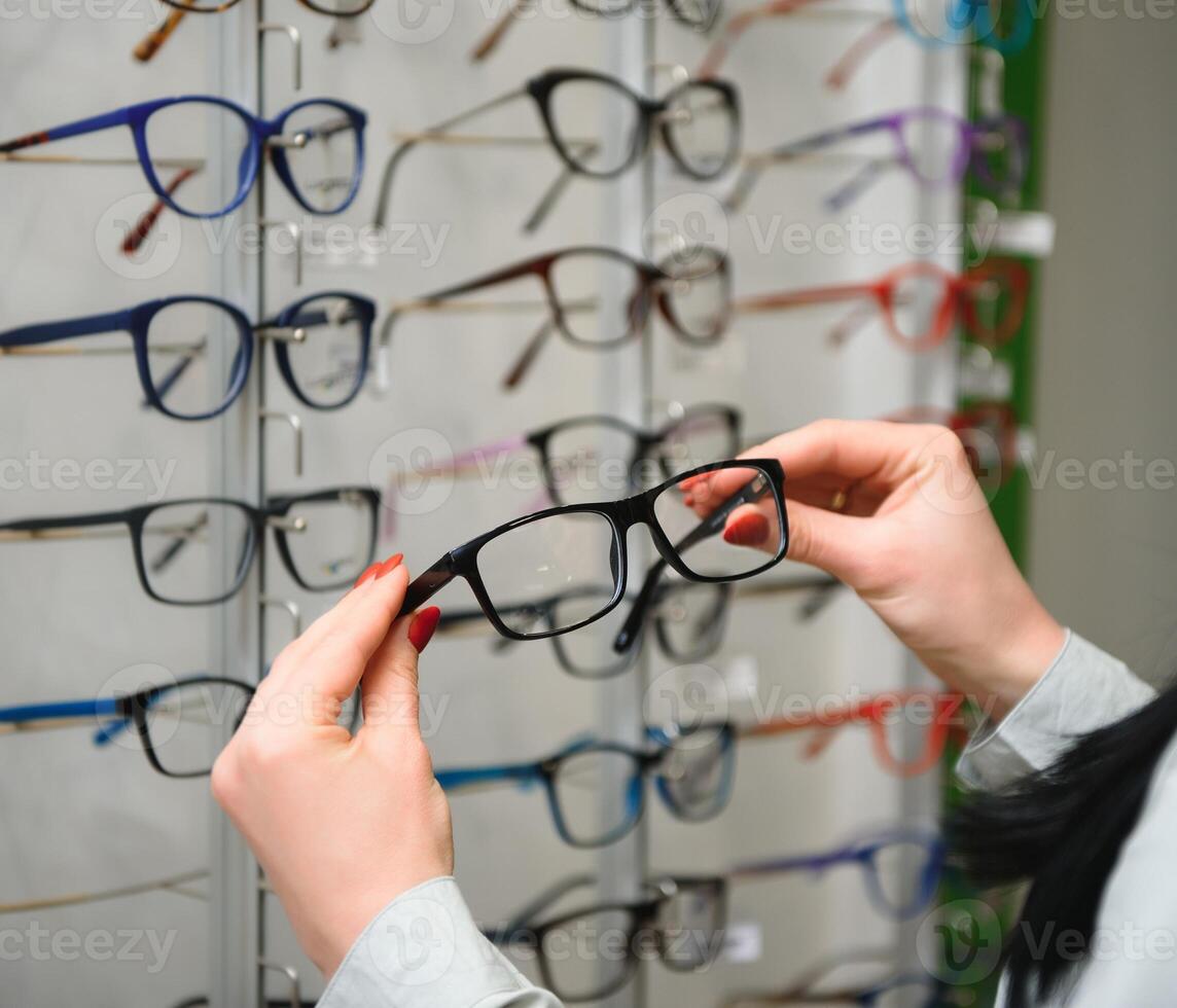 rij van bril Bij een opticiens. bril winkel. staan met bril in de op te slaan van optiek. vrouw hand- kiest bril. gezichtsvermogen correctie foto