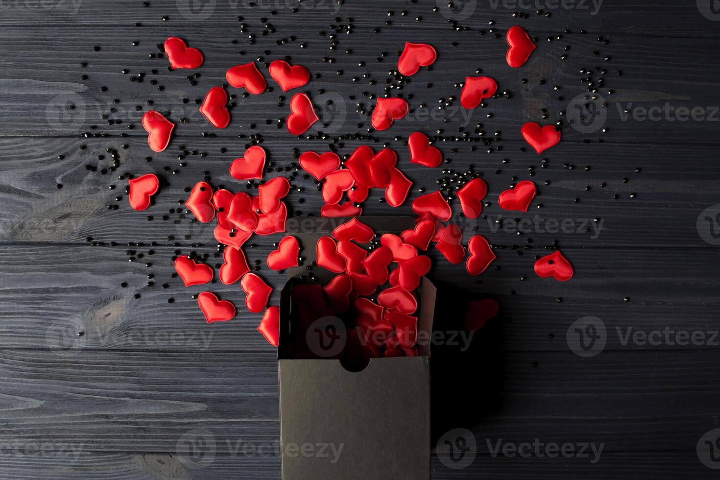 rood harten zijn gegoten uit van een zwart geschenk doos Aan een donker blauw houten tafel. foto