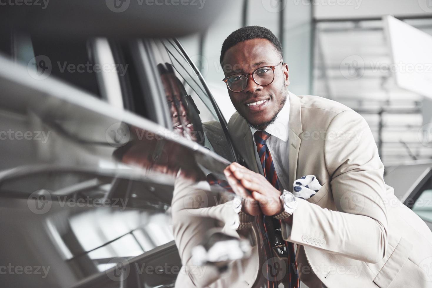 knappe zwarte man bij de dealer knuffelt zijn nieuwe auto en lacht foto