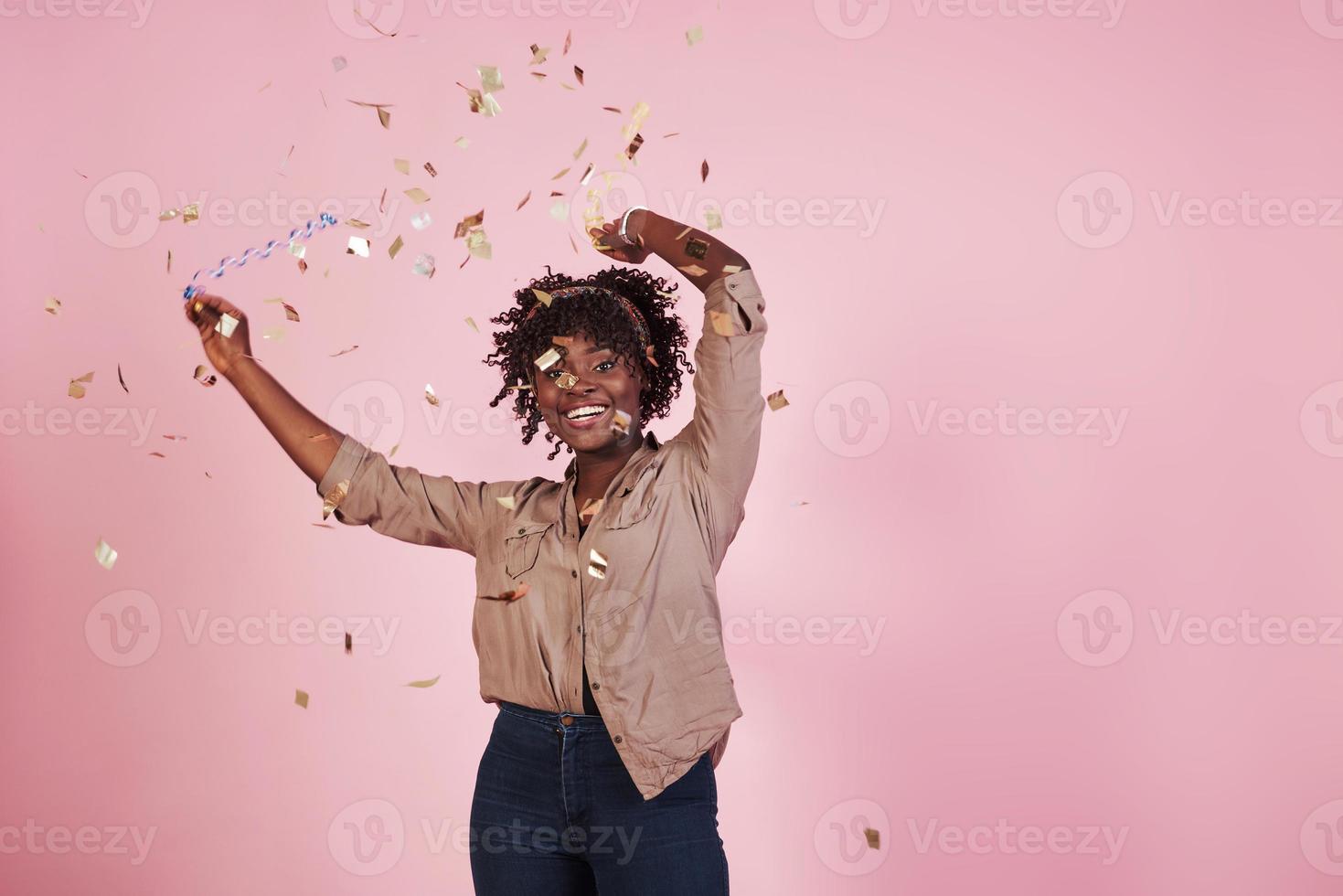 partij conceptie. de confetti in de lucht gooien. afro-amerikaanse vrouw met roze achtergrond erachter foto