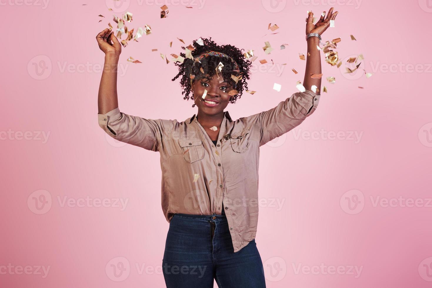 de confetti in de lucht gooien. afro-amerikaanse vrouw met roze achtergrond erachter foto
