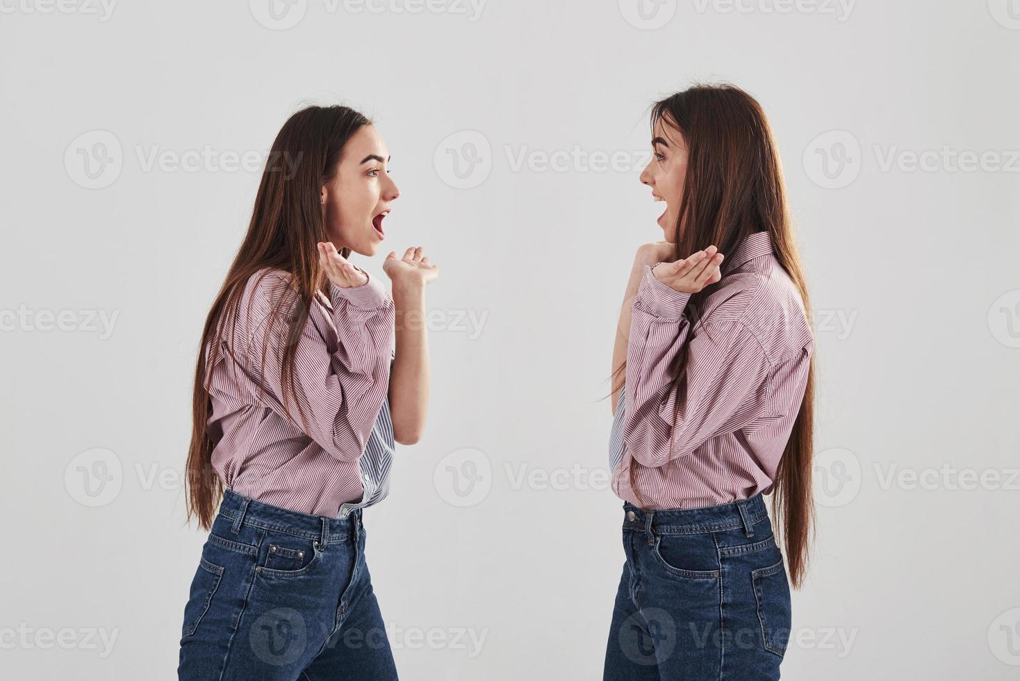 ze kijken elkaar aan en het lijkt bijna op een spiegel. twee zussen tweeling staan en poseren in de studio met witte achtergrond foto