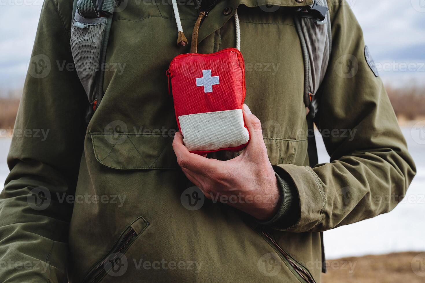 een toerist persoon houdt in zijn hand- een eerste steun uitrusting, een rood medisch zak voor Spoedgevallen, Gezondheid zorg, een wit kruis, camping apparatuur. foto