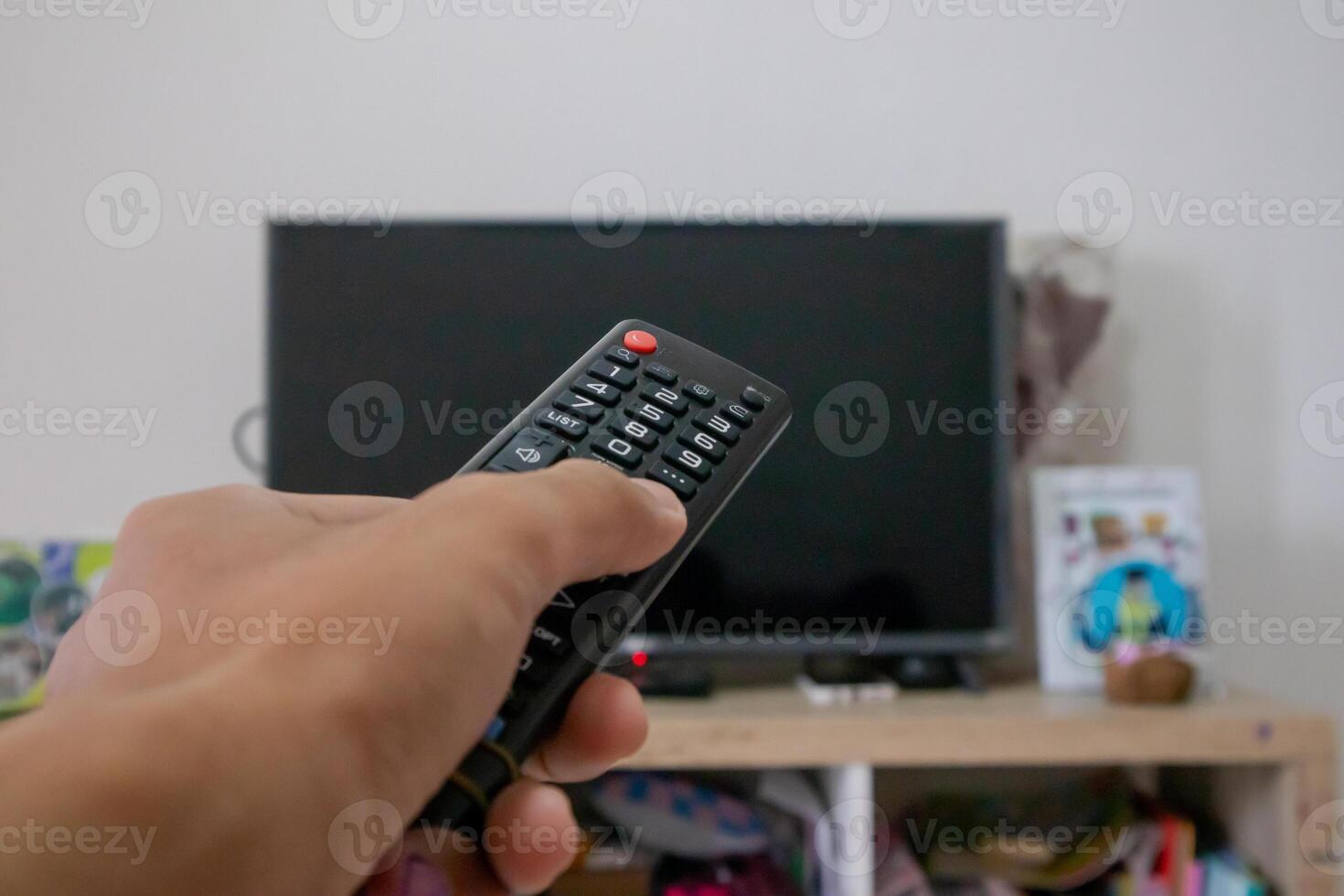 mannetje hand- Holding TV afgelegen controle geregisseerd Aan de televisie binnen de kamer foto