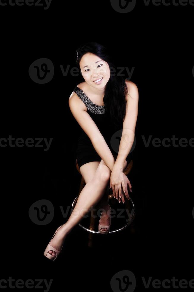 aantrekkelijk Japans Amerikaans vrouw zittend in jurk Aan stoel foto