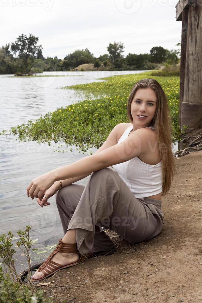 blond Kaukasisch vrouw buitenshuis zittend langs rivier- foto