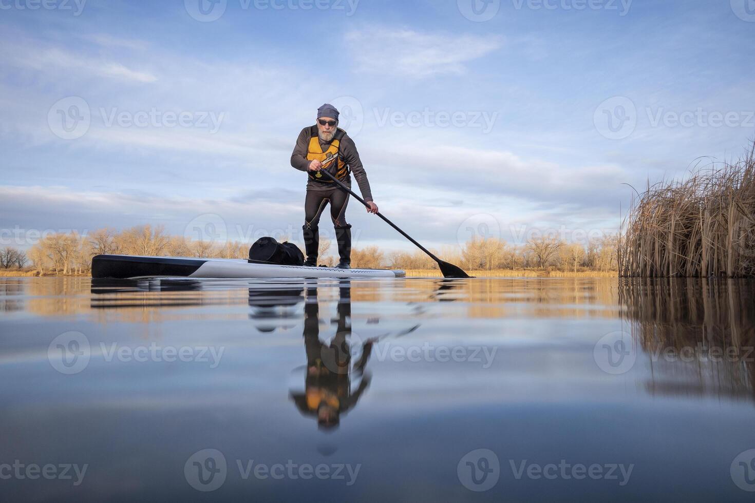 senior peddelaar Aan zijn paddleboard Aan meer in winter of vroeg voorjaar in Colorado, kikker perspectief, gedeeltelijk ondergedompeld actie camera foto