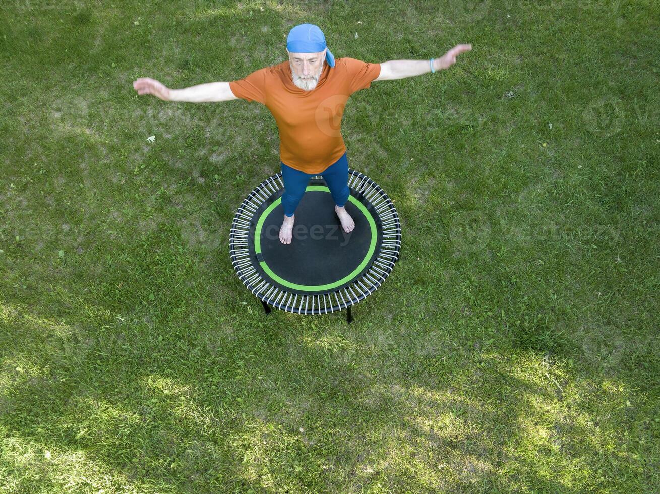 senior te zwaar mannetje oefenen Aan een mini trampoline in zijn achtertuin achtertuin, geschiktheid en terugkaatsend concept, antenne visie foto