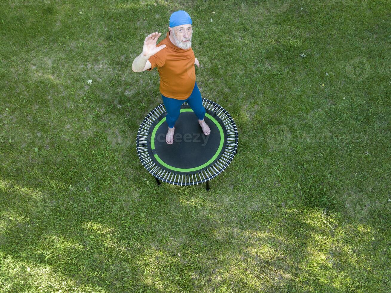 senior te zwaar mannetje oefenen Aan een mini trampoline in zijn achtertuin achtertuin, geschiktheid en terugkaatsend concept, antenne visie foto