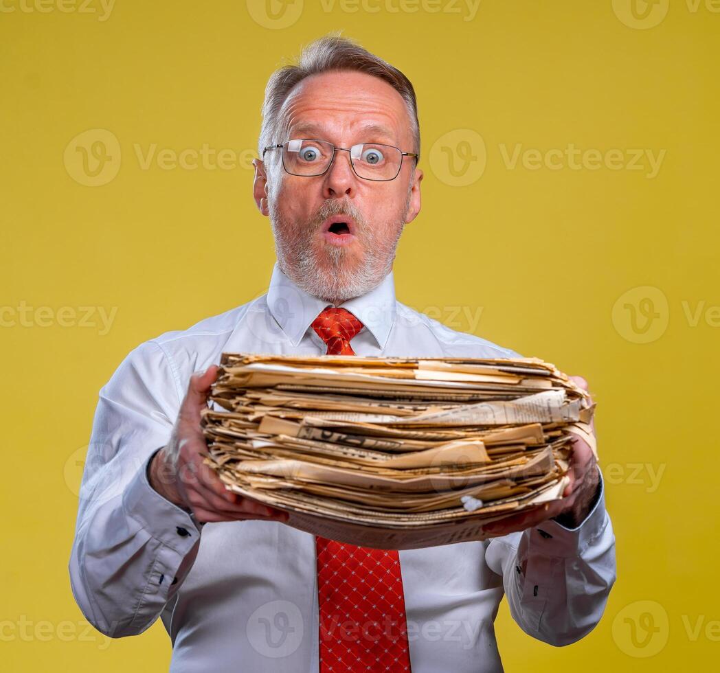 gefrustreerd uitvoerend arbeider over- geel achtergrond overwerkt Holding aambeien van documenten papier werk. foto