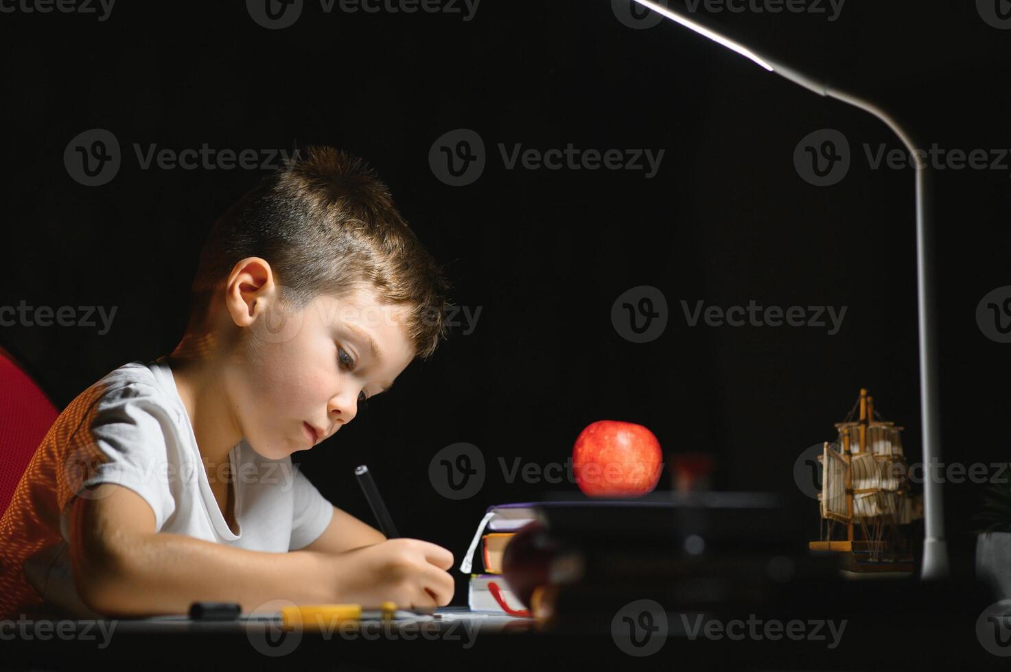 jongen leren lessen in de huis instelling Bij de tafel in de licht van een tafel lamp. foto