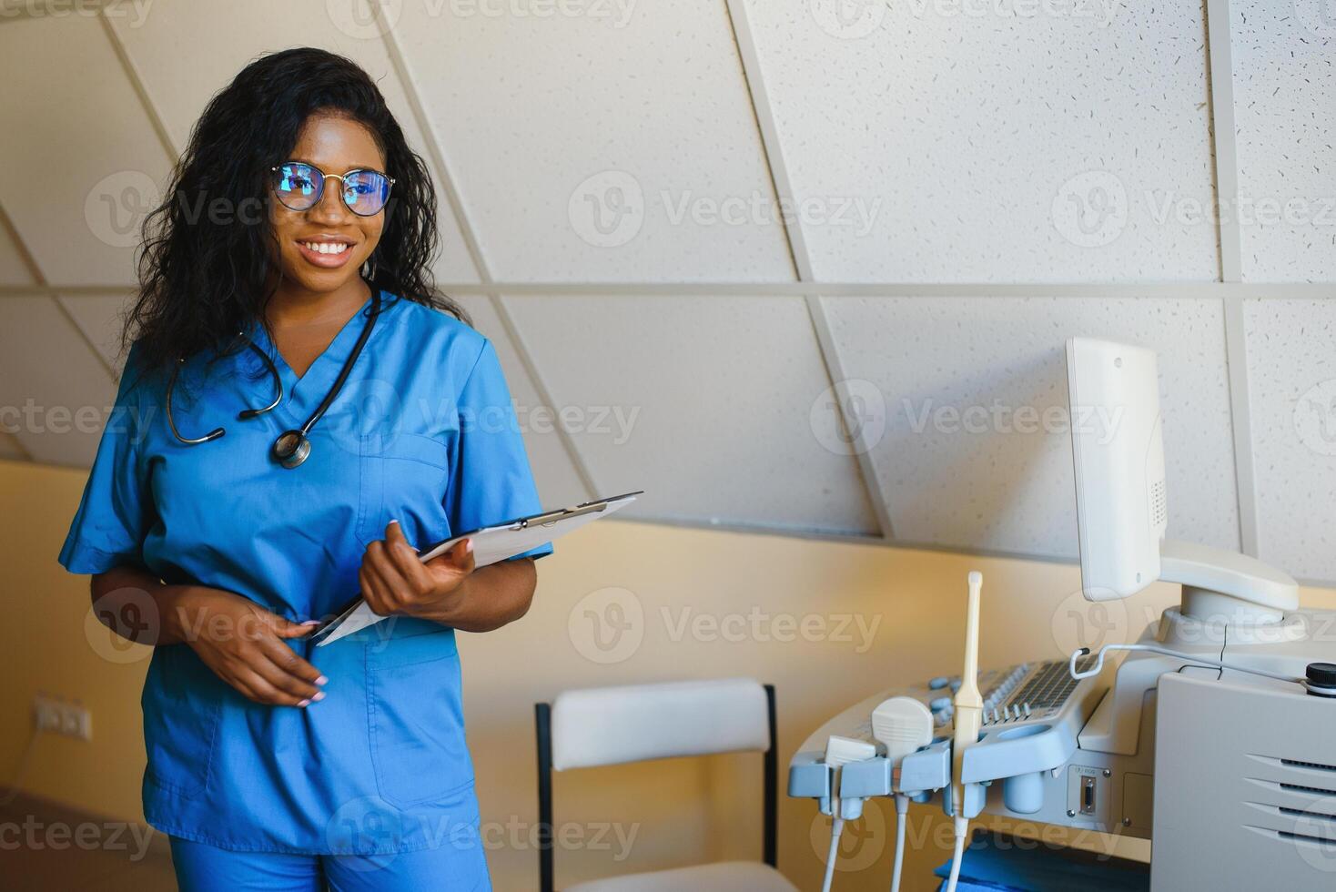 jong afro Amerikaans vrouw dokter staand in kliniek kantoor in de buurt modern echografie machine. foto