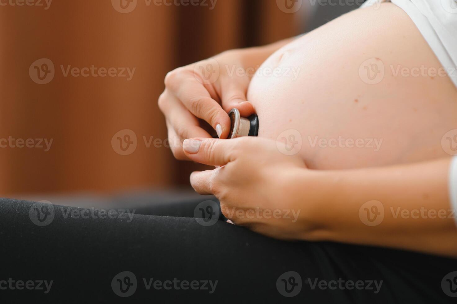 zwanger vrouw gebruik makend van stethoscoop onderzoeken haar buik Aan bank, gelukkig zwanger vrouw concept. foto