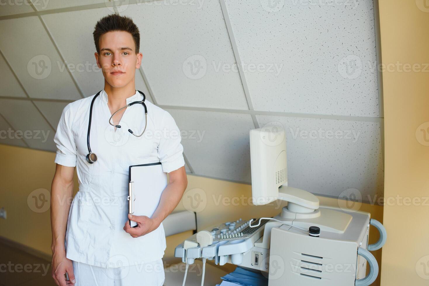 charmant jong mannetje dokter , zittend Bij zijn kantoor in de buurt echografie scannen machine. knap vriendelijk dokter genieten van werken Bij de ziekenhuis, kopiëren ruimte. ultrasoon concept foto