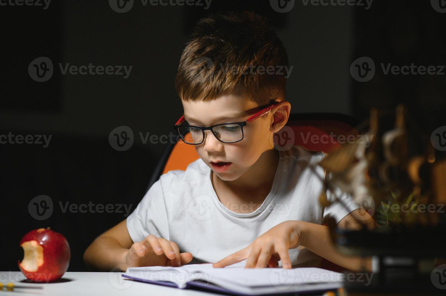jongen leren lessen in de huis instelling Bij de tafel in de licht van een tafel lamp. foto