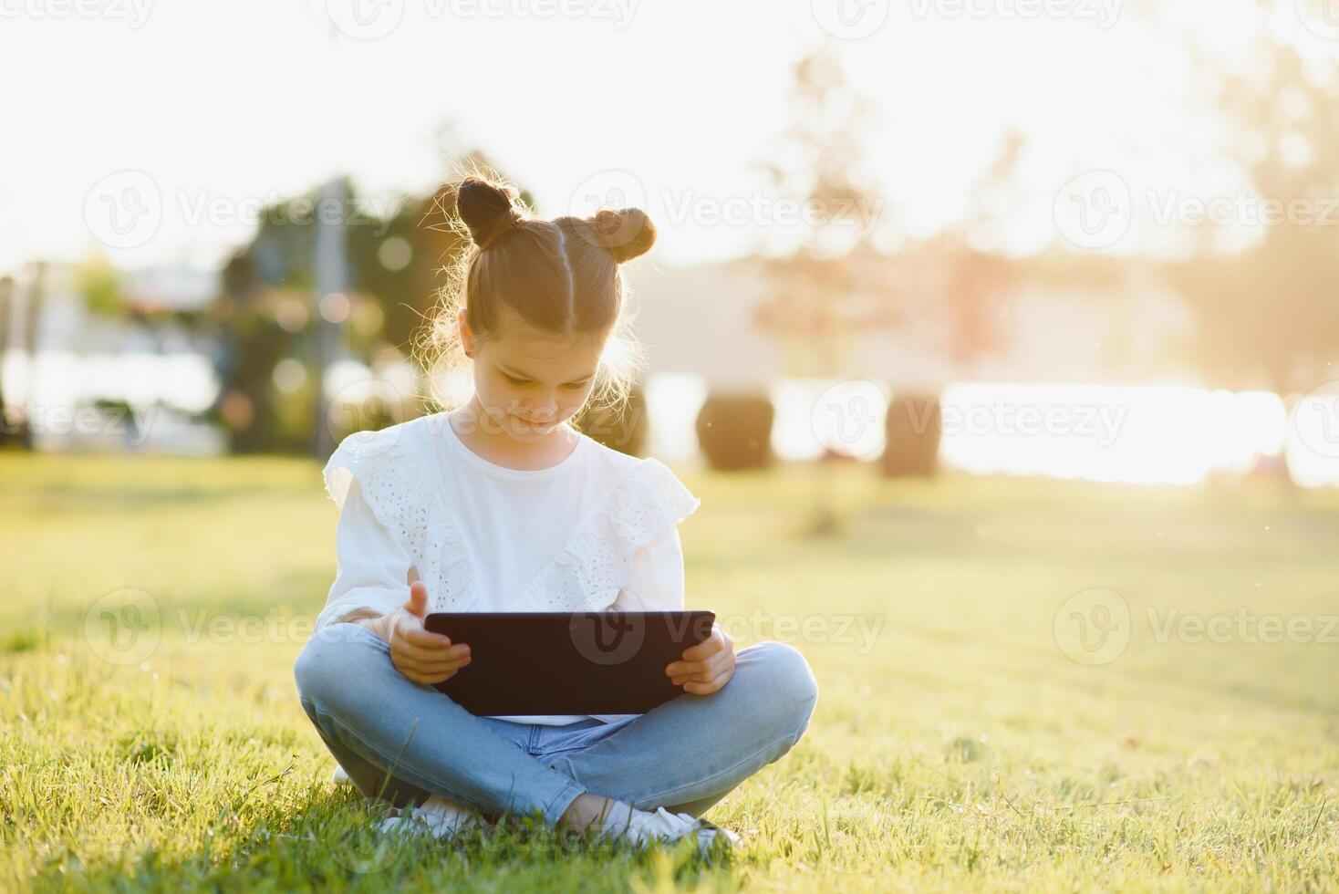 kind met tablet pc buitenshuis. weinig meisje Aan gras met computer foto