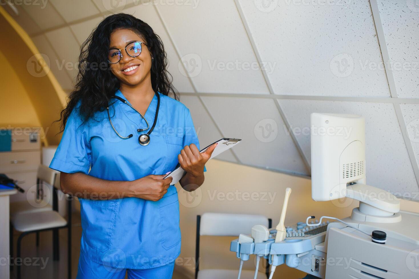 jong afro Amerikaans vrouw dokter staand in kliniek kantoor in de buurt modern echografie machine. foto