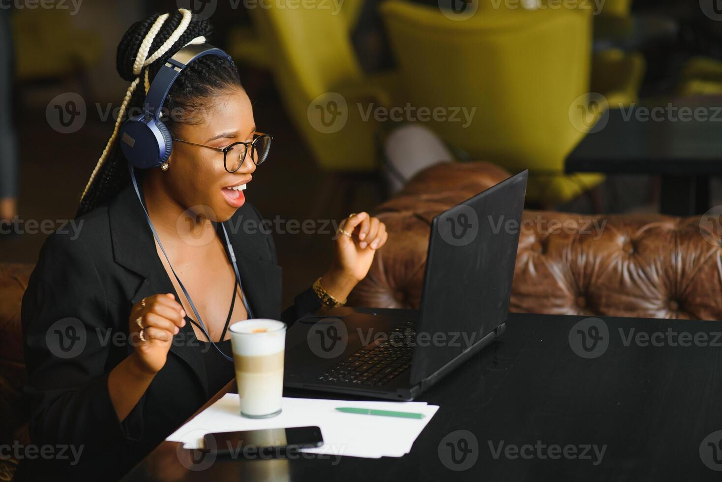 gelukkig zwart meisje in draadloze hoofdtelefoons aan het studeren online, gebruik makend van laptop en nemen notities, cafe interieur, kopiëren ruimte foto