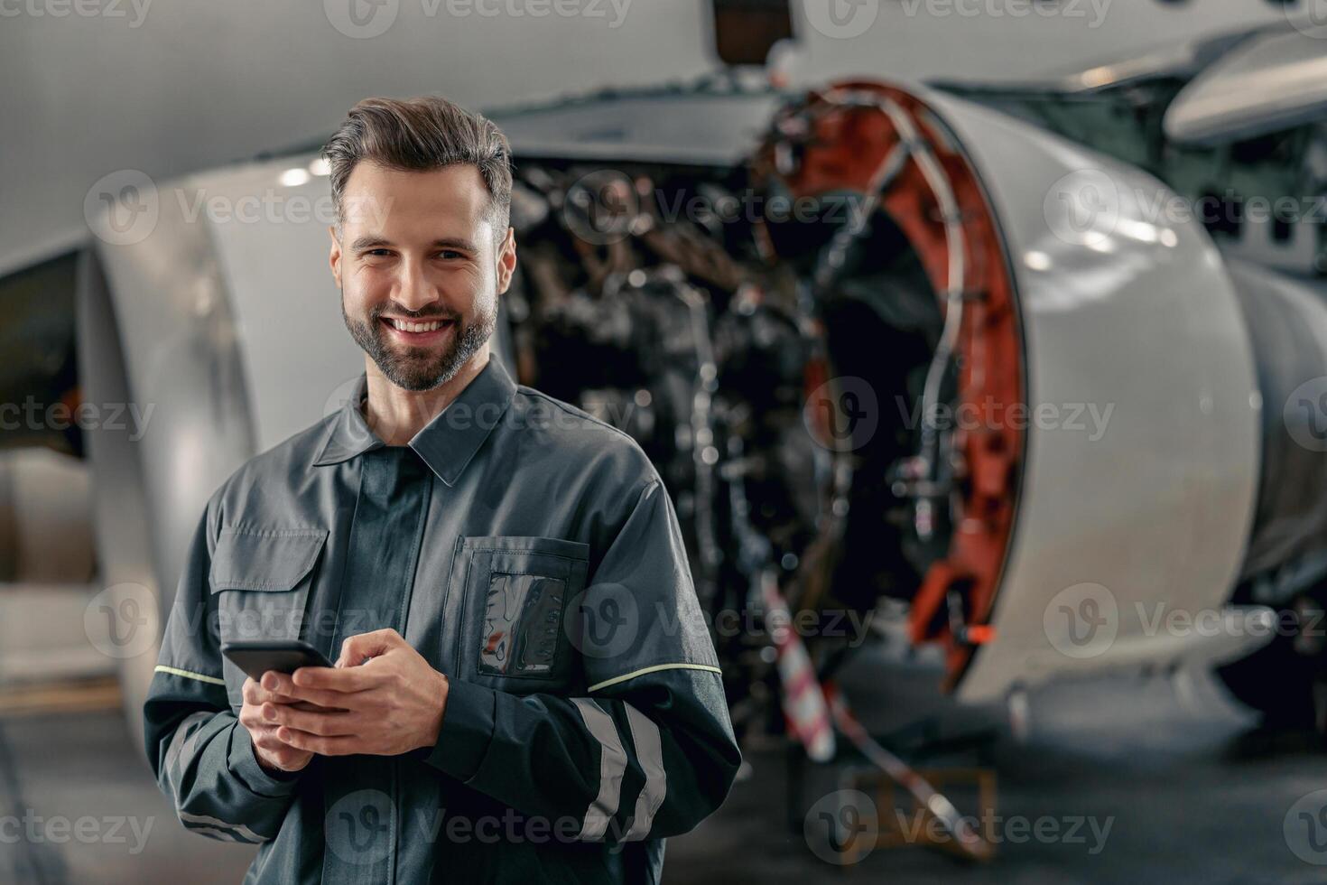 vrolijk vliegmaatschappij monteur gebruik makend van mobiel telefoon in hangar foto