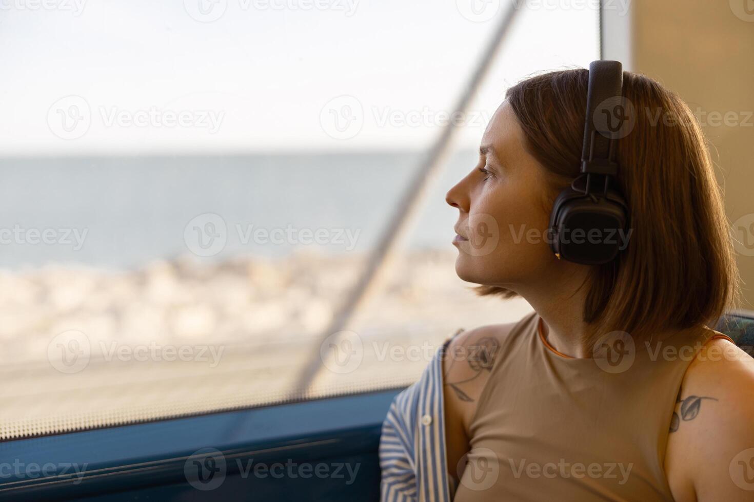 vrouw in hoofdtelefoons terwijl op reis in openbaar vervoer en op zoek visie buiten de venster foto