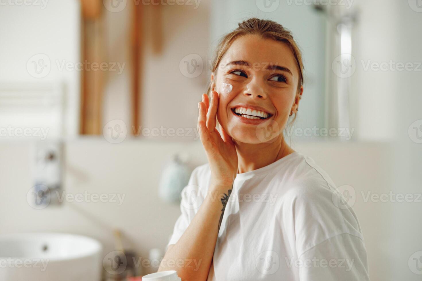 jong mooi vrouw nemen zorg van huid door toepassen vochtinbrengende crème room in badkamer foto