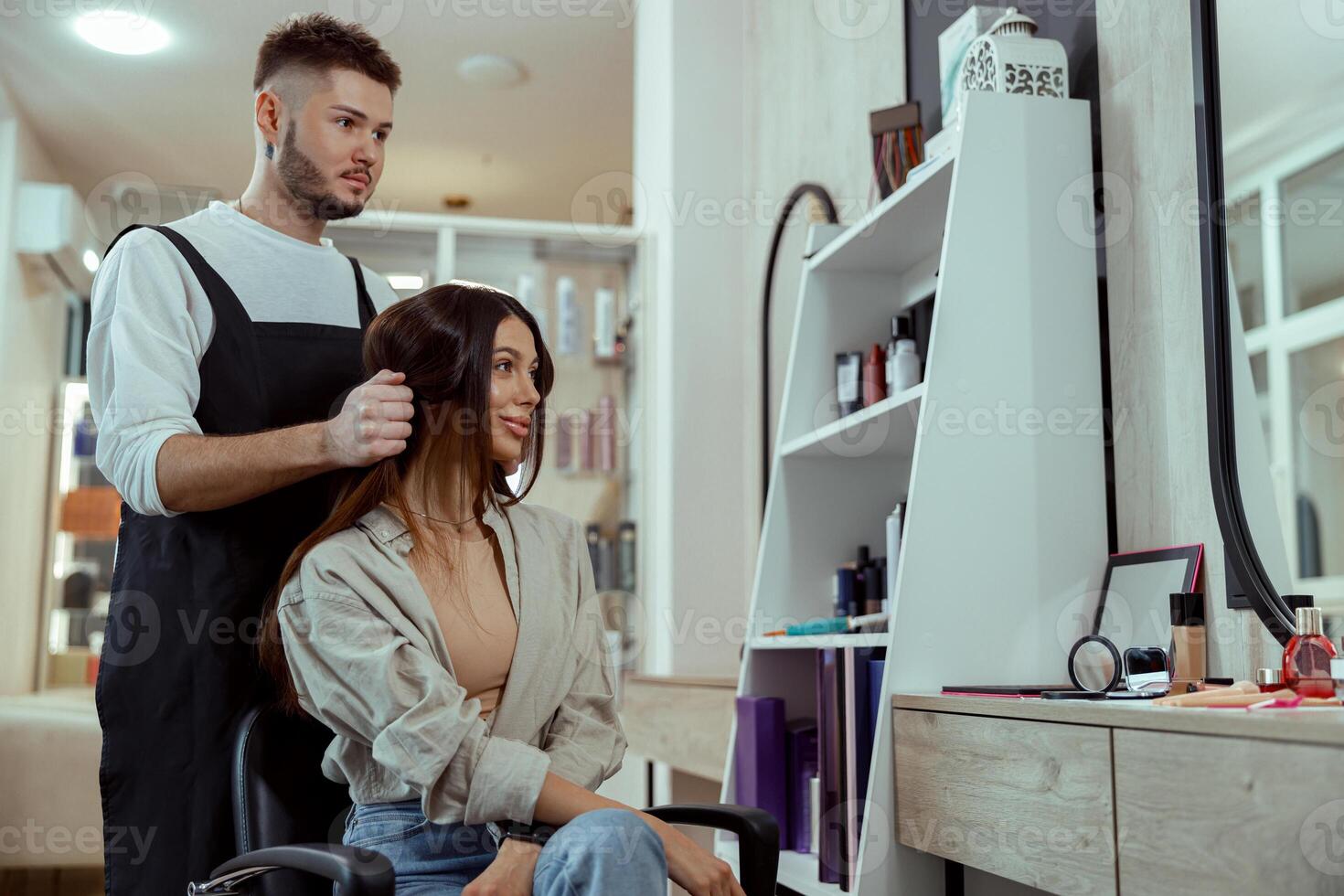 mooi vrouw met lang haar- op zoek verheugd terwijl haar stylist aan het doen haar haar- Bij schoonheid salon foto