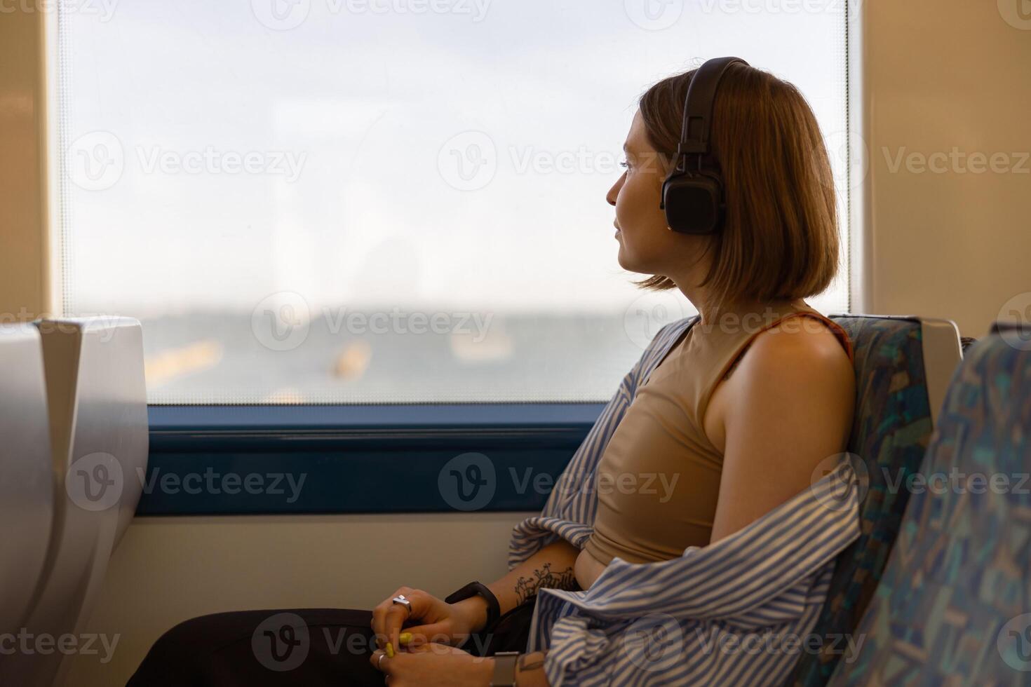 vrouw in hoofdtelefoons terwijl op reis in openbaar vervoer en op zoek visie buiten de venster foto