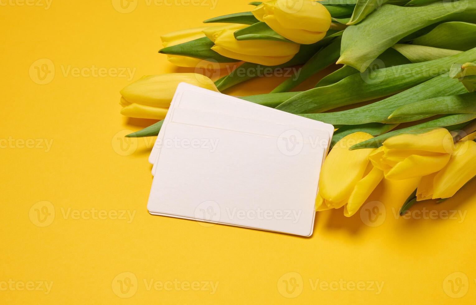 blanco papier wit bedrijf kaart en een boeket van geel tulpen Aan een geel achtergrond foto