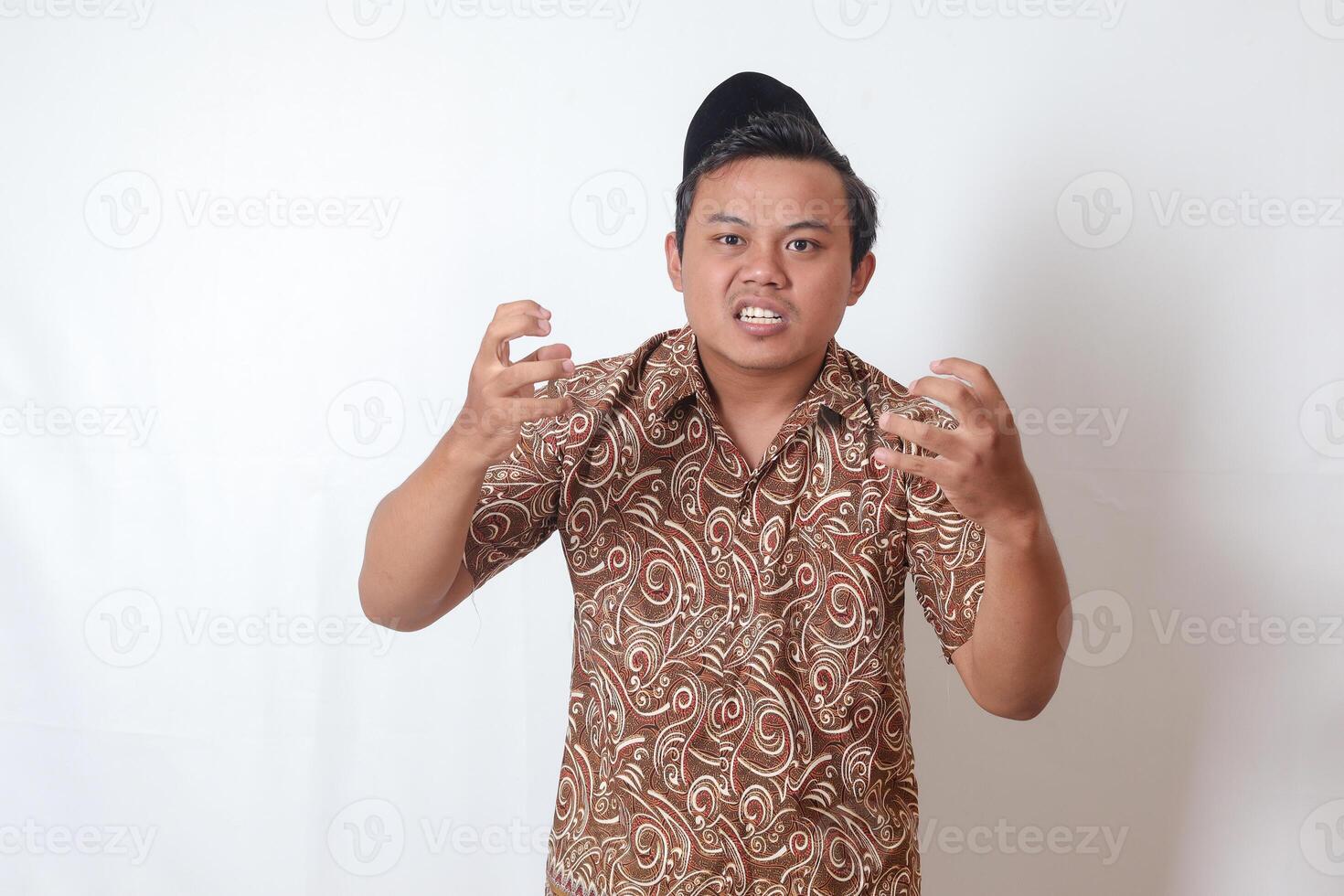 portret van geërgerd Aziatisch Mens vervelend batik overhemd en songkok maken boos hand- gebaar met vingers. geïsoleerd beeld Aan grijs achtergrond foto