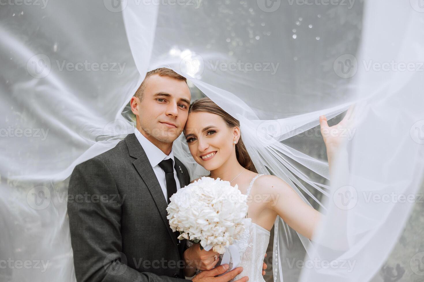 im zo blij ik getrouwd hem. bijgesneden schot van een aanhankelijk jong bruid glimlachen omarmen haar bruidegom onder een sluier Aan hun bruiloft dag. foto