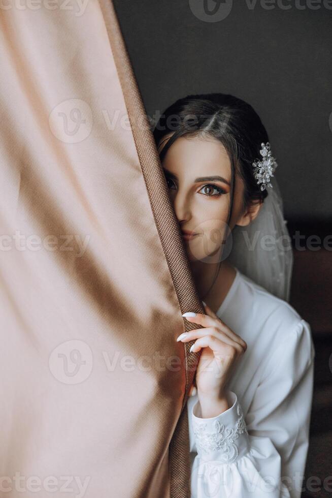 detailopname brunette bruid met mode bruiloft kapsel en verzinnen. een jeugdig bruid met een geavanceerde bruids kapsel binnenshuis door een venster foto