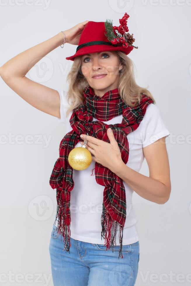 een mooi volwassen vrouw in een Kerstmis rood hoed houdt een gouden Spar bal. foto